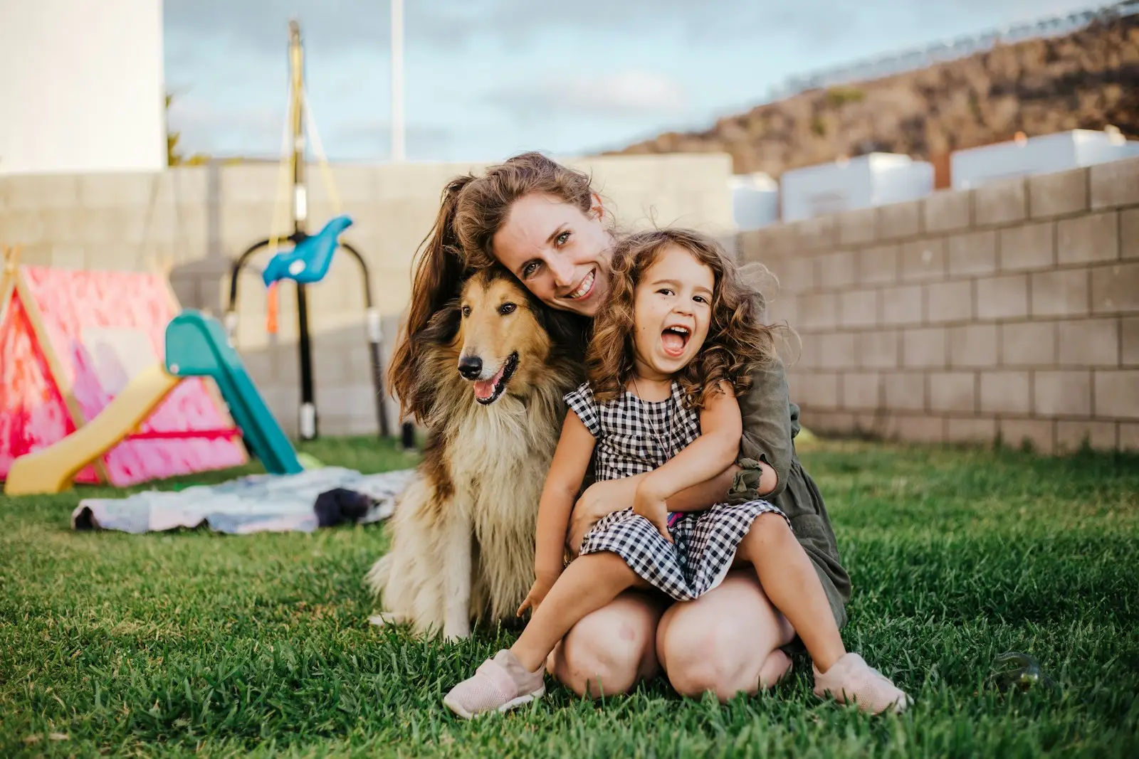 Mamá, niña y collie compartiendo un momento de alegría en el jardín